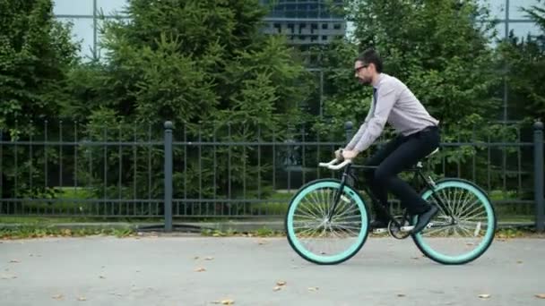 Slow motion of young office worker riding bicycle to work near business center - Кадри, відео