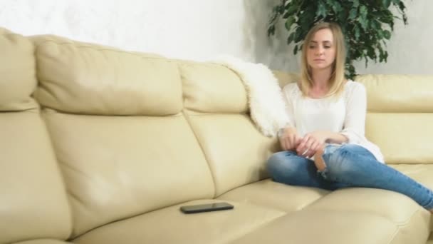 Rozrušená dívka používá doma smartphone, když sedí na gauči. špatná zpráva - Záběry, video