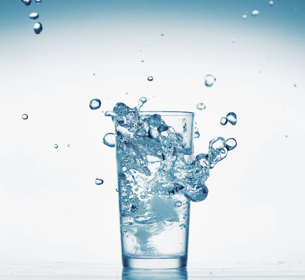 ein Glas Wasser mit Spritzwasser aus fallenden Eiswürfeln, weißer Hintergrund, isoliertes Objekt - Foto, Bild