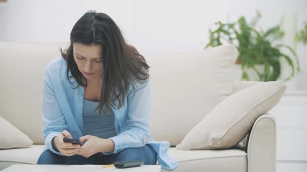 Mujer admirable se concentra en el uso de su teléfono inteligente, mientras está sentado en el sofá, en casa. En cámara lenta. Copiar espacio. 4K
. - Metraje, vídeo