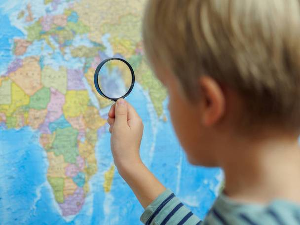 der Junge betrachtet die Landkarte durch eine Lupe - Foto, Bild