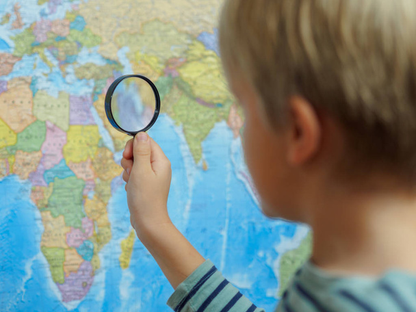 El niño mira el mapa a través de una lupa
 - Foto, Imagen