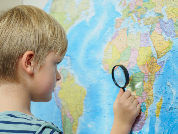 El niño mira el mapa a través de una lupa
 - Foto, imagen