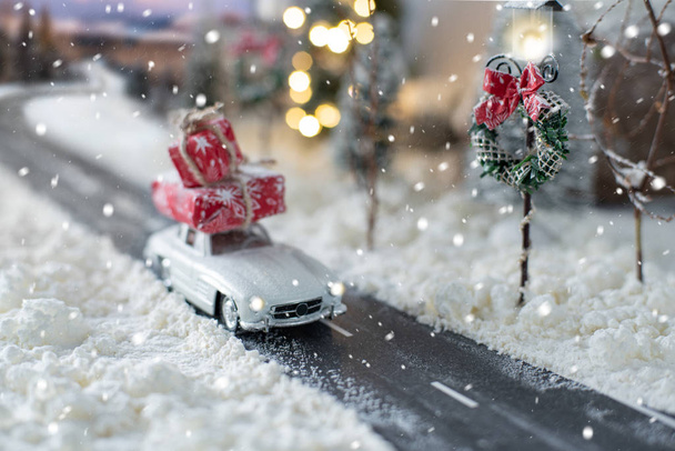 Voiture classique miniature portant un cadeau de Noël sur un paysage hivernal enneigé
 - Photo, image
