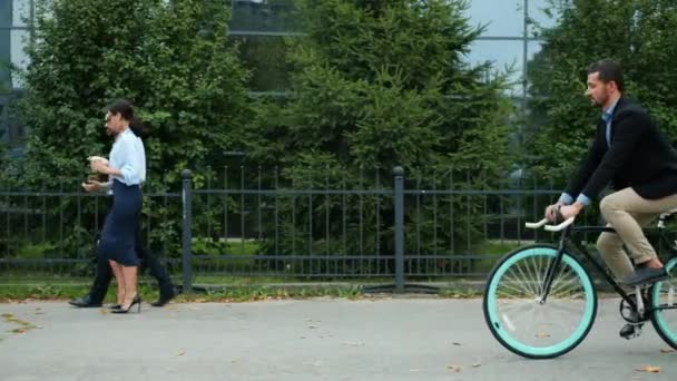 Handsome active businessman riding bike to office building in summer morning - Video, Çekim