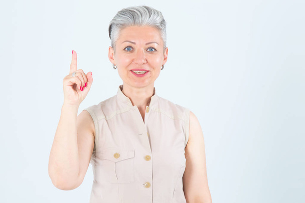 Good idea! Middle aged woman points a finger up, standing on a gray background. - Foto, afbeelding