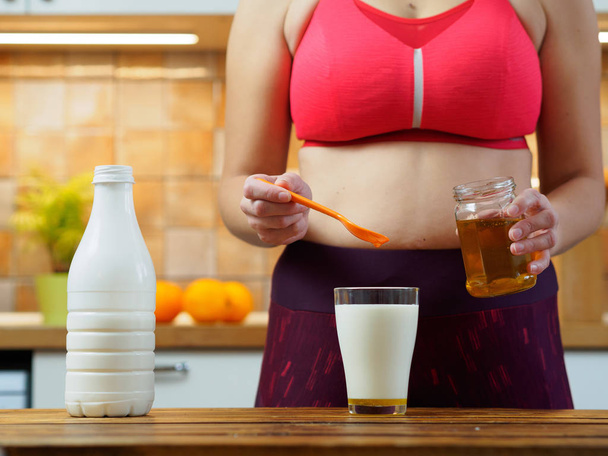 Sporty girl puts honey in a glass of almond milk, slow motion - Photo, Image