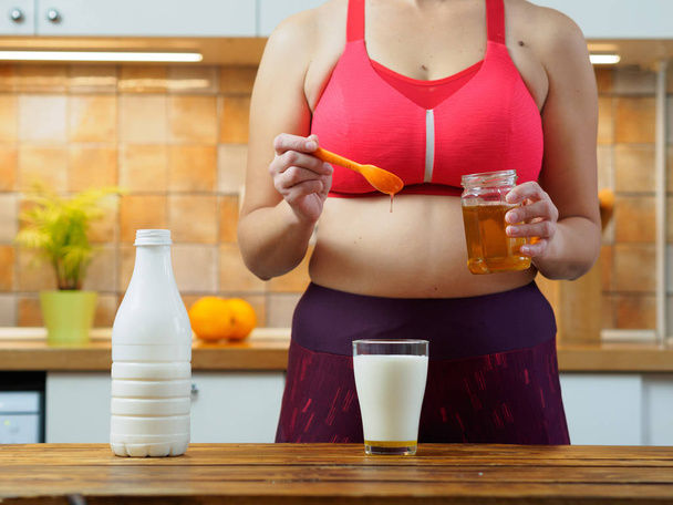 Sporty girl puts honey in a glass of almond milk, slow motion - Фото, зображення