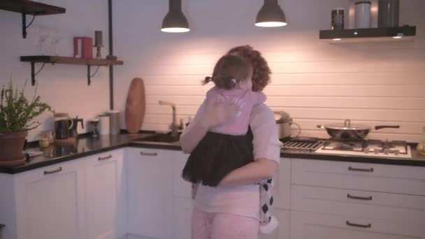 Little girl fooling around in the kitchen. Mom and daughter have fun together. Mom is circling her daughter. The girl is crawling around mom. Mom and daughter have fun in the kitchen. - Video
