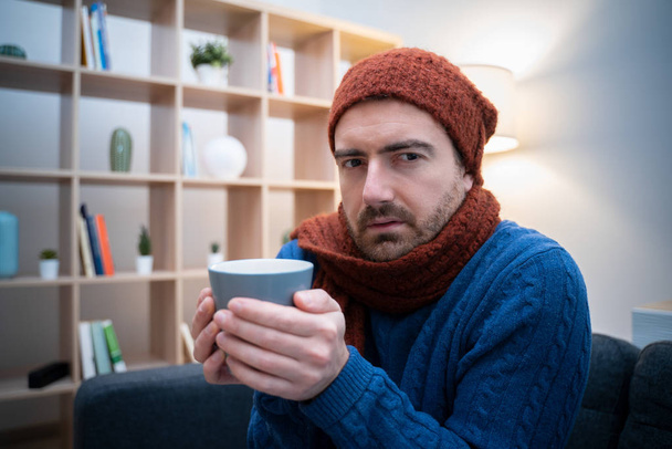 Мужчина чувствует себя очень холодно дома с теплой одеждой
 - Фото, изображение