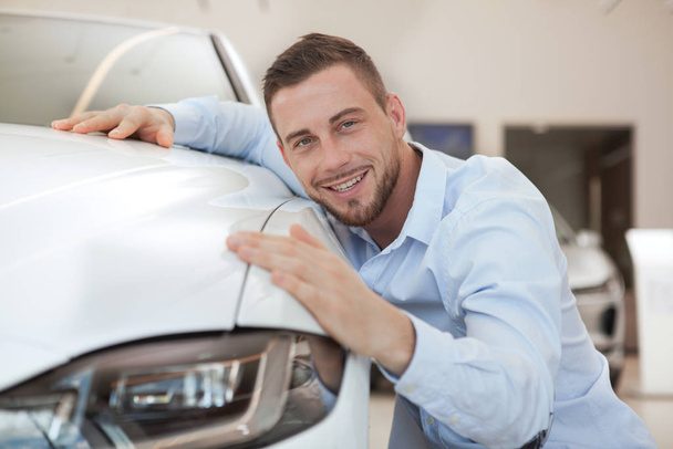 Handsome young man buying a new car at dealership salon - Foto, afbeelding