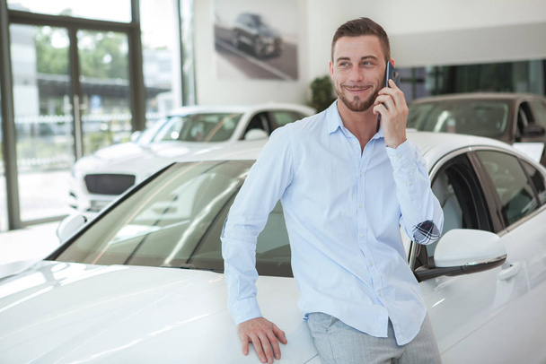 Handsome young man buying a new car at dealership salon - Фото, изображение