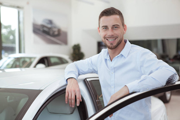 Handsome young man buying a new car at dealership salon - Foto, Bild