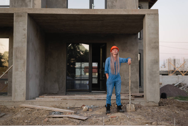Woman worker with a shovel stands at a construction site. Background - Fotó, kép