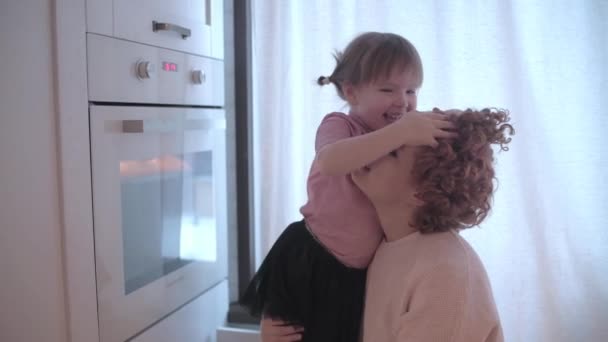 Little girl fooling around in the kitchen. Mom and daughter have fun together. Mom is circling her daughter. The girl is crawling around mom. Mom and daughter have fun in the kitchen. - Záběry, video