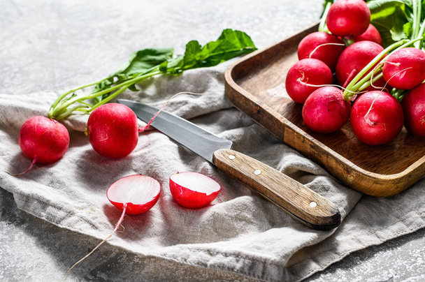 Fresh radishes with tops in a wooden bowl. Farm organic vegetables. Gray background. Top view - Photo, Image