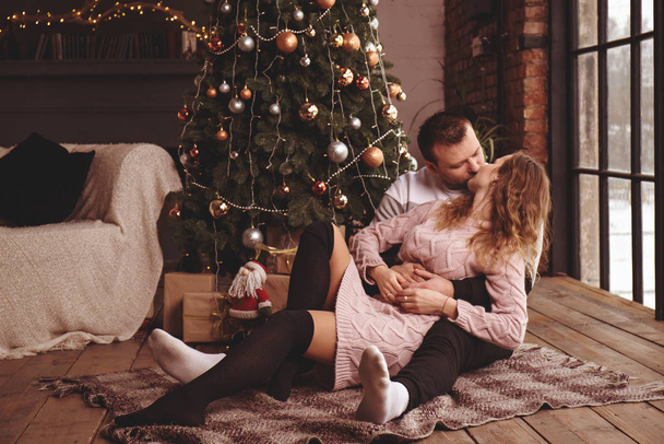 Pareja cariñosa besos cerca del árbol de Navidad en el suelo
 - Foto, imagen