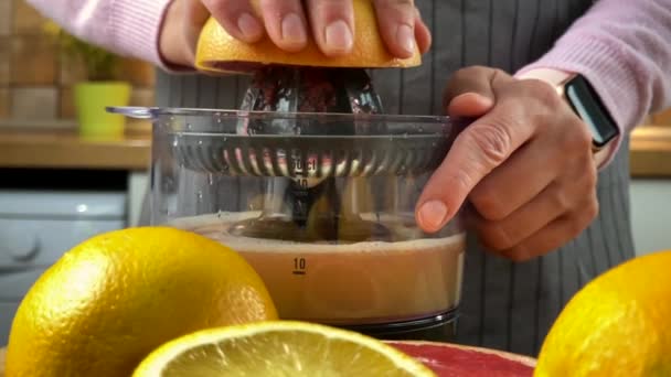 Egy nő a konyhában citruslevet présel egy elektromos facsaróval. - Felvétel, videó