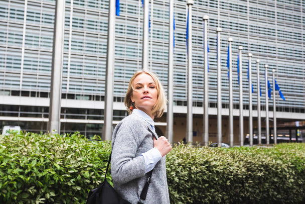 A young woman stands against the backdrop of the European Commission headquarters in Brussels, Belgium - Photo, Image