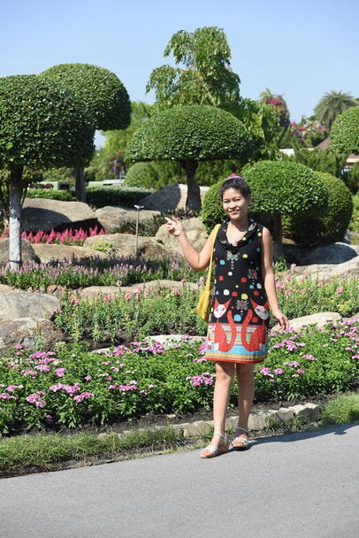 junge Asiatin posiert tagsüber in floralem Park mit bunten Blumen   - Foto, Bild
