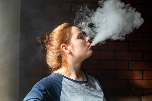 Vaping teenager with  problem skin. Portrait of young cute girl smoking an electronic cigarette in the bar. Bad habit that is harmful to health. Vape activity. - Foto, imagen