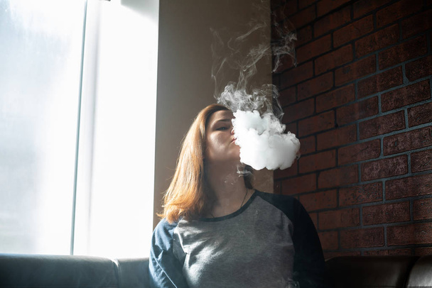 Vaping teenager with  problem skin. Portrait of young cute girl smoking an electronic cigarette in the bar. Bad habit that is harmful to health. Vape activity. - Zdjęcie, obraz