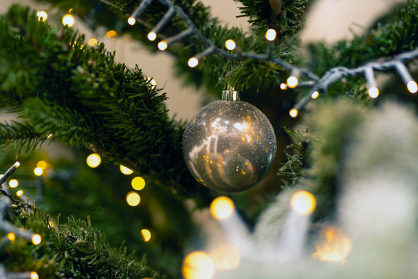One bright ball hanging in the green christmas tree, close-up christmas decoration background - Photo, Image