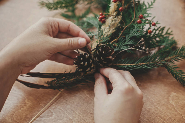 Rustykalny świąteczny wieniec. Ręce trzymające szyszki sosnowe, Berrie - Zdjęcie, obraz