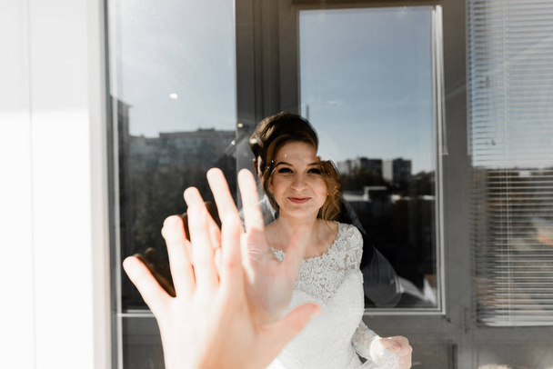 Portrait of young gorgeous bride on the balcony. Wedding day gatherings. Beautiful girl dresses and gathers for a wedding ceremony in apartaments while waiting for the groom. Bride's morning - Фото, изображение