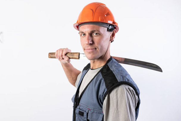 A builder with a short katana on his shoulder. Repairman wearing a helmet and work clothes. - Photo, Image
