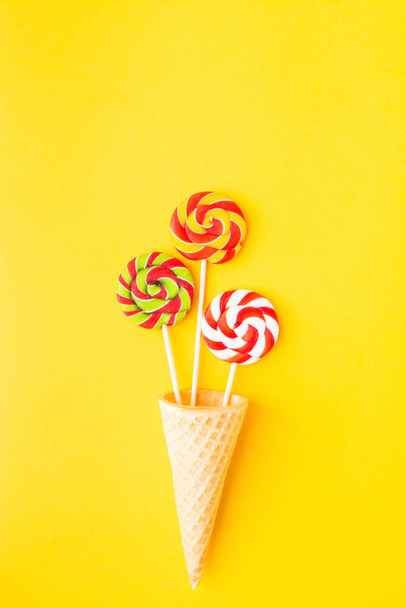 Three colorful candies on stick in waffle cone over yellow background with copy space. Top view. Flat lay - Valokuva, kuva