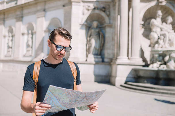 Ο άνθρωπος τουρίστας με ένα χάρτη της πόλης και σακίδιο στην οδό Ευρώπης. Καυκάσιος αγόρι ψάχνει με χάρτη της Ευρωπαϊκής πόλης. - Φωτογραφία, εικόνα