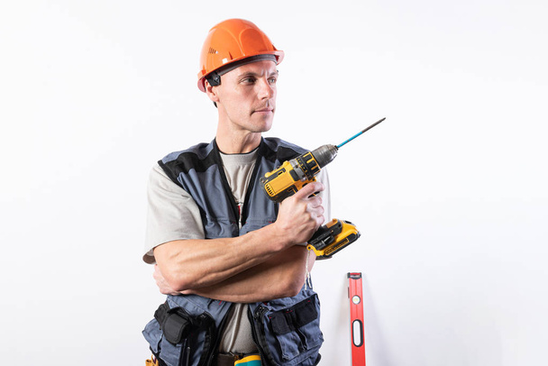Builder repairman holding a drill like a gun. In a helmet and work clothes. - Foto, afbeelding