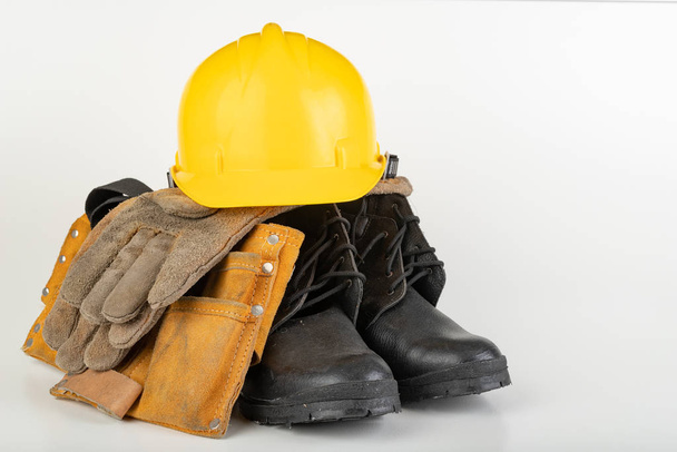 Casco, botas de trabajo y guantes sobre una mesa blanca
.  - Foto, Imagen
