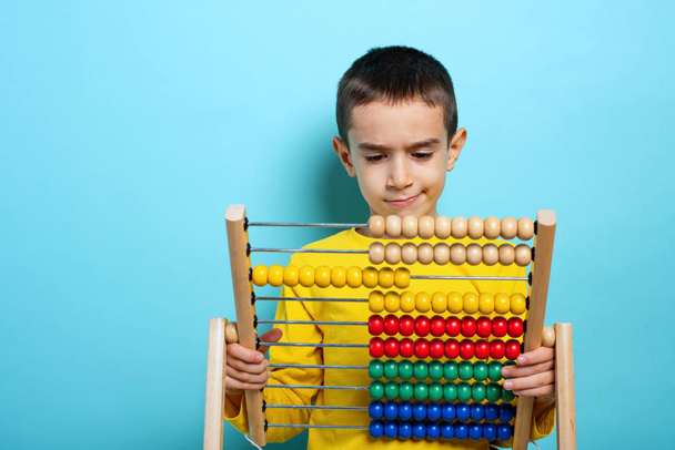 Child tries to solve mathematical problem with abacus. Cyan background - 写真・画像