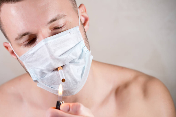 a man without clothes in a medical mask lights a cigarette, close up - Φωτογραφία, εικόνα
