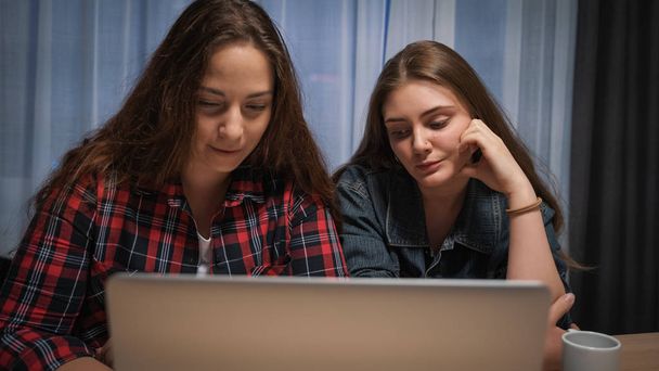 Dos chicas novias utilizan el ordenador portátil en la mesa en casa
 - Foto, imagen