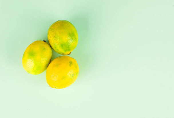 Τρία ώριμα κίτρινα λεμόνια σε φόντο μέντας. - Φωτογραφία, εικόνα