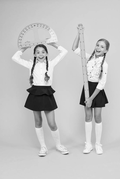 Formula. back to school. Maths and geometry. Kids in uniform at yellow wall. friendship and sisterhood. happy small girls study mathematics. students use protractor ruler. stem disciplines - Фото, изображение