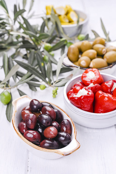 Traditional appetizers, olives from Greek cuisine. White wood background. View from above. Fresh branches of olives. Copy space. - Фото, изображение