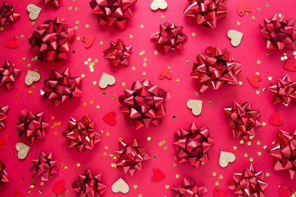Red bows and heart shaped golden glitter, over red background, flat lay. Party, birthday, Christmas or Valentine's Day pattern. Flat lay. - Foto, immagini