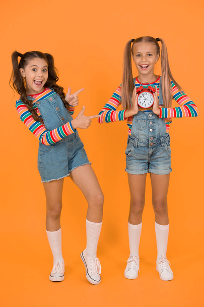 Timing personal plan and schedule. Counting time concept. Dead line. Happy little girls hold vintage alarm clock on orange background. Small children smiling with mechanical clock. School clock - Photo, image