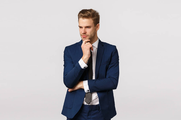 Thoughtful smart and focused young blond bearded man in formal classic suit, having deep thought, touching chin look away, thinking about solution, make plan, brainstorm during meeting - Photo, Image