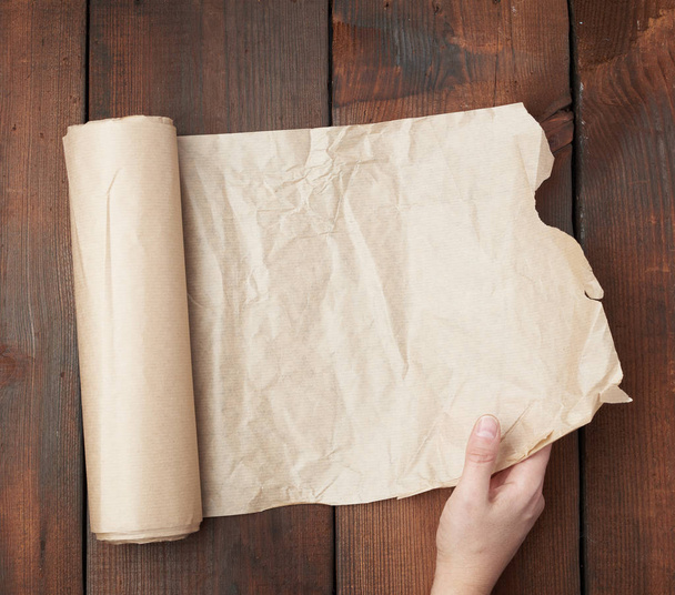 hand holds unfolded roll with brown parchment paper on wooden ba - Foto, Imagem