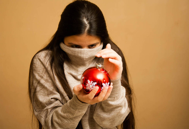 Girl wrapped up in a sweater with a Christmas ball - Foto, imagen