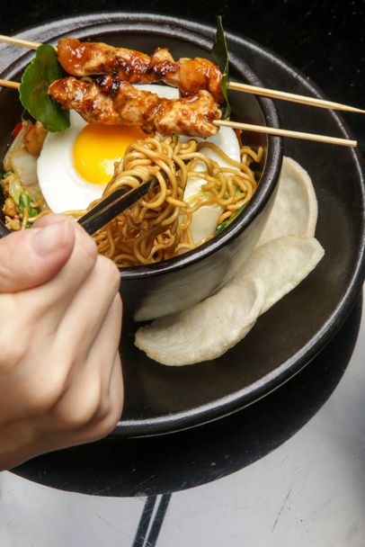 Fried egg noodles and vegetables served with chicken satay. Creative restaurant meal concept. - 写真・画像