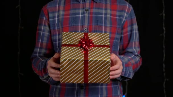 Αγόρι με κουτί δώρου σε μαύρο φόντο. κουτί δώρου με κορδέλα για Καλή Χρονιά, Καλά Χριστούγεννα, Ημέρα του Αγίου Βαλεντίνου, γενέθλια - Πλάνα, βίντεο
