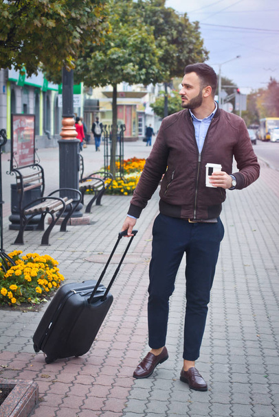 Handsome man with a suitcase for tourism. Exit the house for travel. Fashionably dressed guy and coffee. Stock Photo. - Fotografie, Obrázek