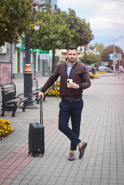 Handsome man with a suitcase for tourism. Exit the house for travel. Fashionably dressed guy and coffee. Stock Photo. - Foto, Imagem