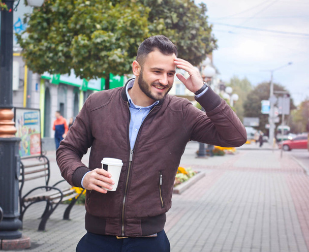 Man in a jacket and suit on a European street with coffee in his hands. Business guy fashion clothes. Autumn landscape, portrait. stock photo - Foto, imagen